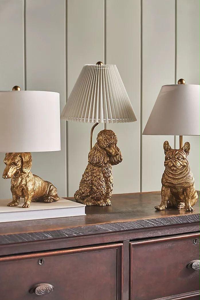 Three gold dog-shaped table lamps with pleated shades on a sideboard