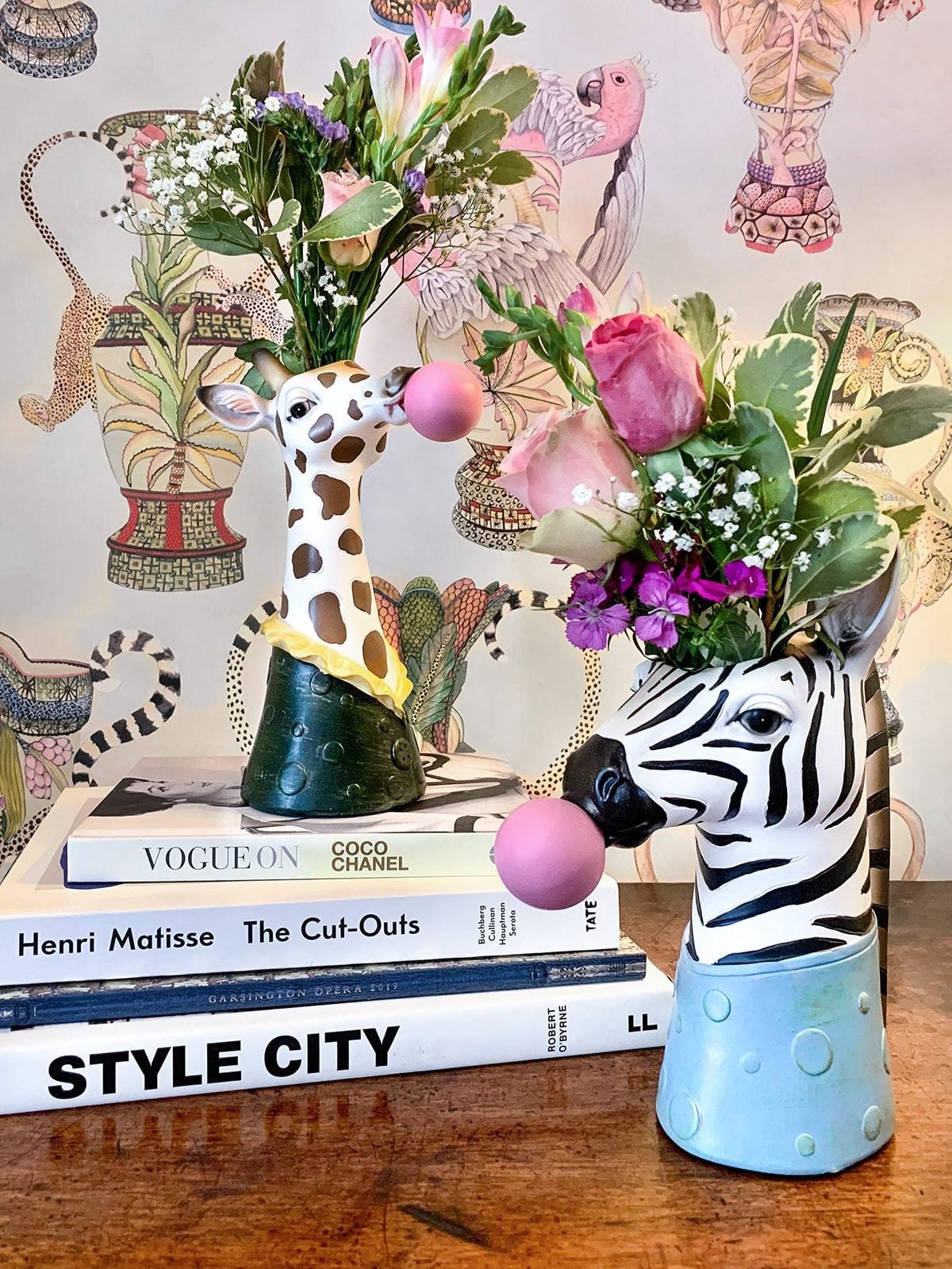 Giraffe and zebra head vases filled with flowers on a stack of books
